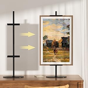 Wandmontiertes Bildaufhängesystem mit schwarzer vertikaler Stange und horizontalen Halterungen. Gelbe Pfeile weisen auf Befestigungspunkte neben gerahmten Kunstwerken hin.