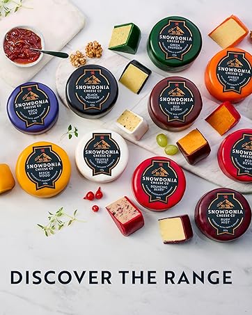 Collection of artisanal cheese wheels in various colored wax coatings, displayed with fruit, nuts and preserves on a light surface. Text reads 'Discover the Range'.