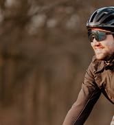 Close-up outdoor cycling shots showing cyclists in action, wearing dark athletic gear against a blurred natural background.