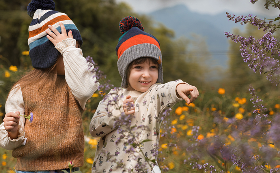 Outdoor autumn scene with colorful wildflowers and two people wearing warm weather attire including knit hats