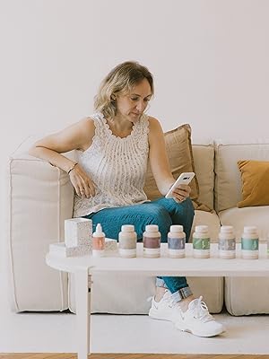 Collection de petits contenants de produits aux couleurs pastel disposés sur une table blanche à côté d'un canapé beige