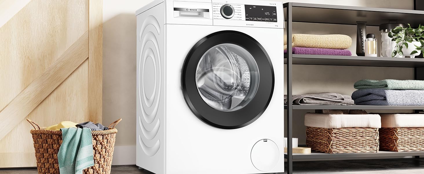 Modern front-loading washing machine in white, shown in a laundry room setting with storage shelves and baskets.