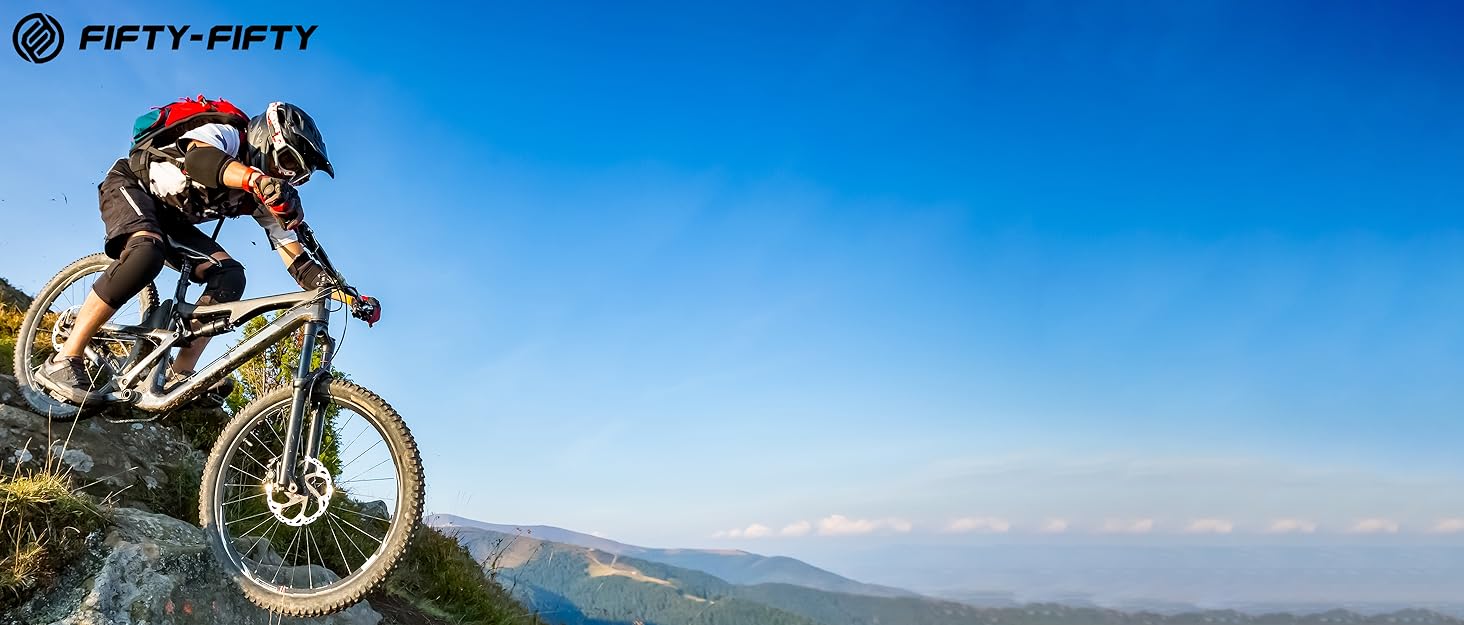 Mountain biker in full gear riding downhill on a rocky terrain against a blue sky and distant landscape.