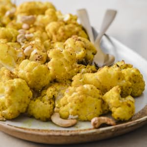 ROASTED CAULIFLOWER WITH CASHEWS AND TURMERIC on a plate with serving spoons.