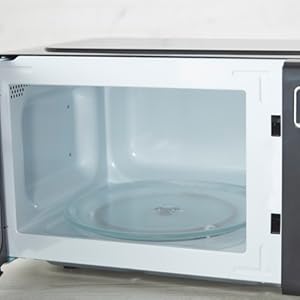 Interior view of a white microwave cavity, showing the glass turntable plate and perforated side walls.