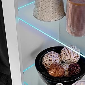 Glasregal mit blauer LED-Beleuchtung an den Kanten, auf dem Dekorationsgegenstände wie geflochtene Kugeln in einer schwarzen Schale und ein strukturierter Lampenschirm ausgestellt