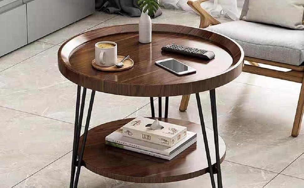 Round wooden coffee table with raised edges, metal hairpin legs, and lower shelf. Table surface holds a cup, phone, and small plant.
