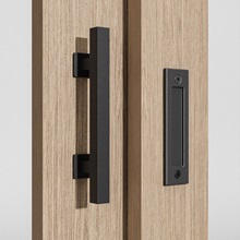 Nahaufnahme von zwei schwarzen Metalltürgriffen oder -griffen, die auf hellem Holz montiert sind. Eine ist eine lange Stange, die andere eine rechteckige Rückplatte