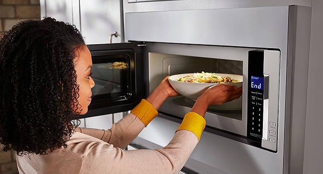 A woman placing a plate of food inside the microwave oven