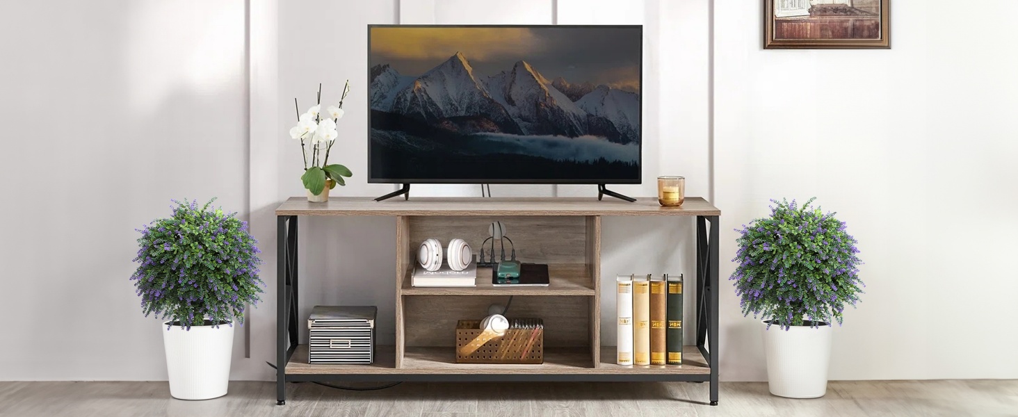 Modern living room setup with floating entertainment center, wall-mounted TV, decorative plants in white planters, and minimal industrial-style furniture against white walls.