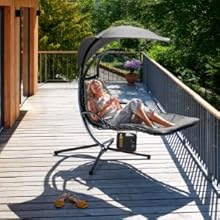 Sedia sospesa da esterno con baldacchino su un ponte di legno. Persona che si rilassa sulla sedia, con alberi visibili sullo sfondo