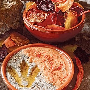 Hummus with a dinosaur footprint in it accompanied by chips. 