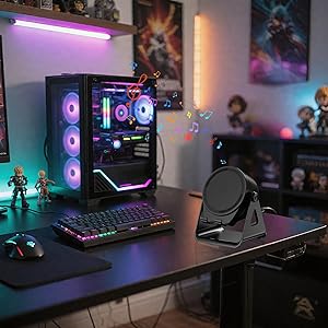 Gaming setup with RGB-lit PC case featuring multiple cooling fans, RGB keyboard, desk fan, and collectible figurines displayed on desk. Purple and orange ambient lighting visible.