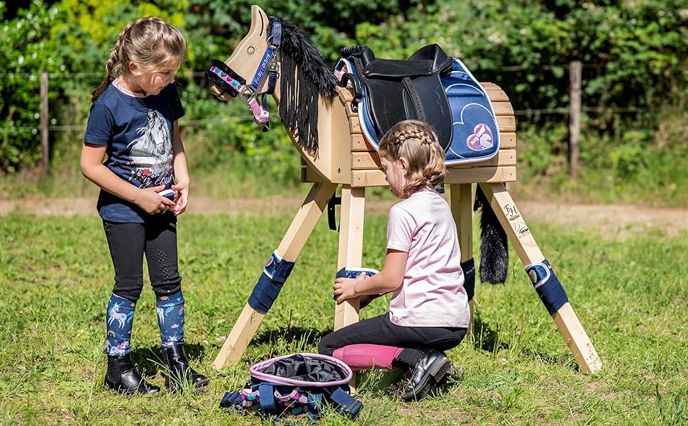 Hölzernes Steckenpferdspielzeug mit schwarzem und blauem Sattel und Beinschützern, positioniert auf Gras im Freien.