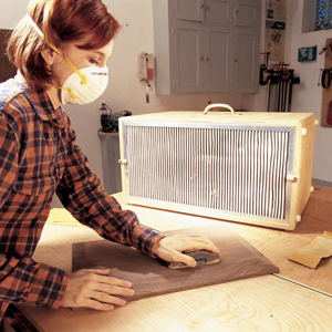 A woman sands wood with an air cleaner beside her