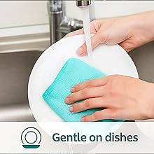 Microfiber cloth gently cleaning a white plate under running water.