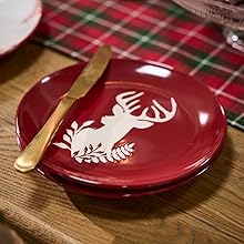Deep red decorative plates with white deer silhouette design, shown from multiple angles on wooden surface. Plates appear to be part of holiday or seasonal dining collection.