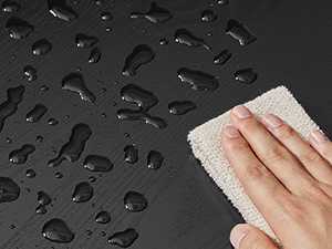 Közeli kép: vízcseppek egy sötét felületen, amelyeket világos színű ruhával törölnek le.