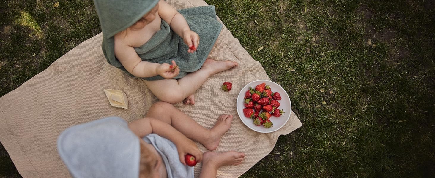 children wearing hooded towels having a picnic and eating strawberries in the garden