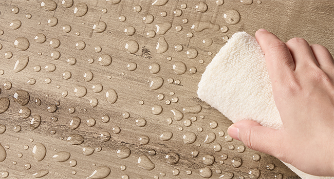 Kvapky vody na textúrovanom hnedom povrchu sa utierajú bielou handričkou alebo špongiou.