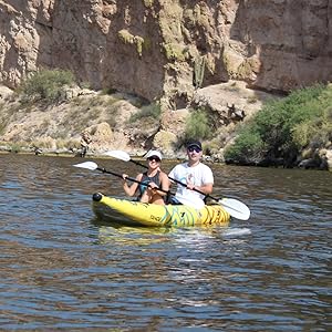 A man and woman with PFD belts on paddling a Buoy Watersports Tandem Tahoe Kayak on a lake