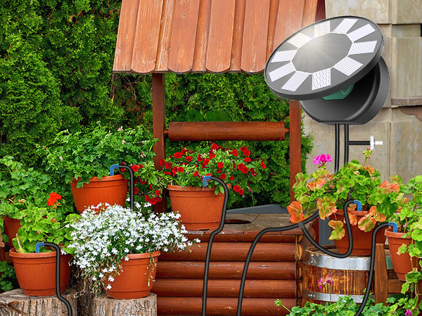 منظره باغ در فضای باز با گلدانهای سفالی پر از گلهای رنگارنگ، یک سازه چوبی و یک چراغ دایرهای خورشیدی.