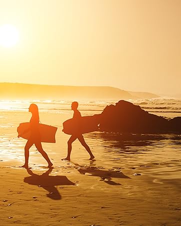 A couple walks along the beach at sunset with their bodyboards 
