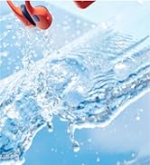 Nahaufnahme von spritzendem klarem Wasser vor hellblauem Hintergrund mit roten Elementen, die in der Flüssigkeit sichtbar sind.