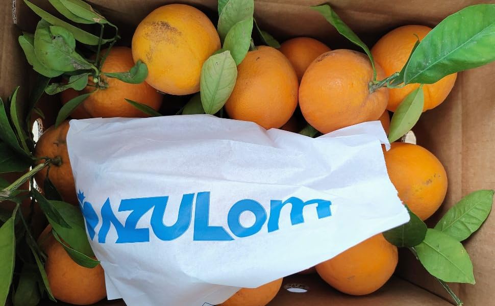Caja de cartón llena de naranjas frescas y hojas verdes, parcialmente cubierta por una bolsa blanca con texto azul que dice «AZULOM