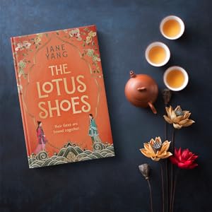 Orange book on dark background next to flowers and teapot and tea