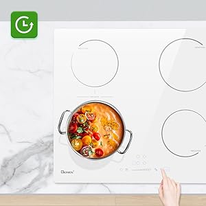 White induction cooktop with a pot of bright orange soup or stew containing vegetables, photographed from above with a hand visible.