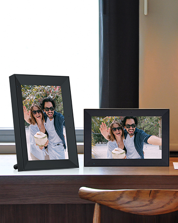 Two black digital photo frames on wooden surface. Larger frame displaying color photo, smaller frame to the left.