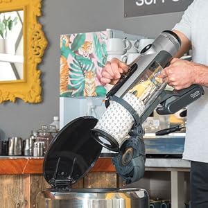 Barista pouring milk into coffee cup in cafe setting. Yellow-framed mirror and 'Thank you for supporting' sign visible in background.