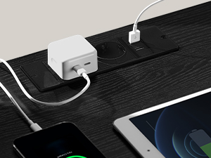 Biely nabíjací adaptér s viacerými USB portami na tmavom drevenom povrchu, ktorý sa pripája k tabletu a iným zariadeniam.