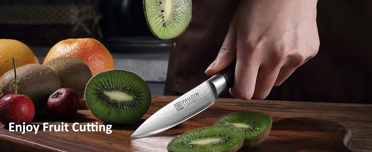Chef's knife cutting kiwi on wooden board. Various fruits in background. Text 'Enjoy Fruit Cutting' visible.