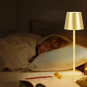 Slanke gouden tafellamp met conische kap die een nachtkastje verlicht. Lampstatieven op nachtkastje bij slapend persoon en open boek