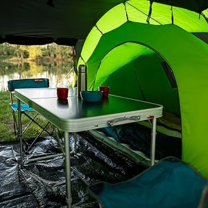 Configuración para acampar que muestra el interior de una tienda de campaña de color verde brillante con una mesa plegable en el interior, con vista a un lago o estanque a través de la abertura de la tienda de campaña.