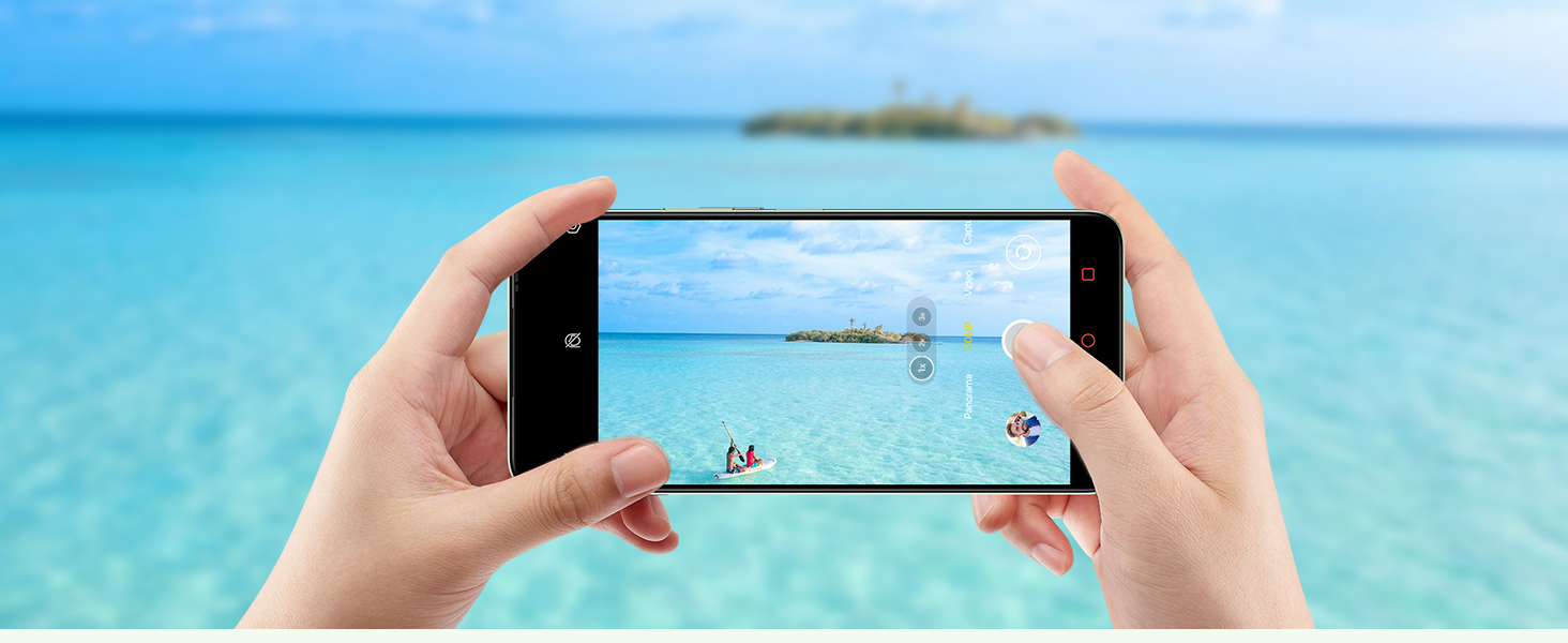 Hands holding smartphone, capturing beach scene. Screen displays people on distant shoreline, demonstrating camera zoom capability.