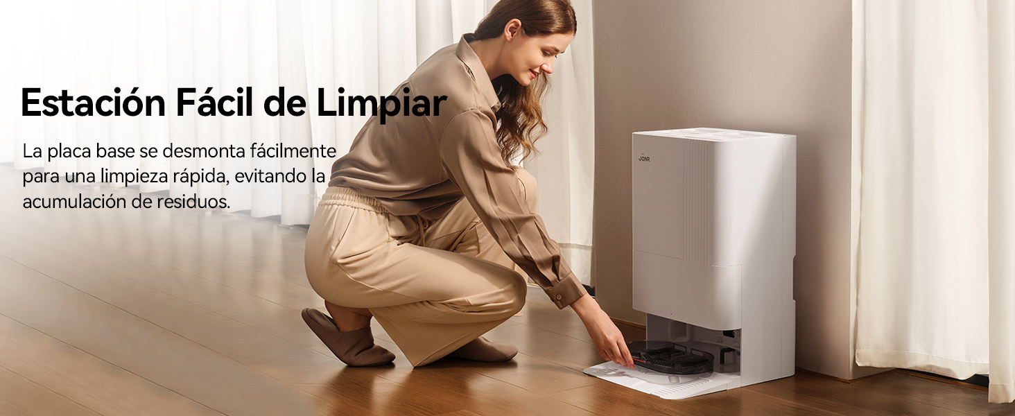 Persona que limpia debajo de un dispositivo blanco en el suelo, demostrando un diseño fácil de limpiar. El dispositivo parece ser una estación o base electrónica compacta