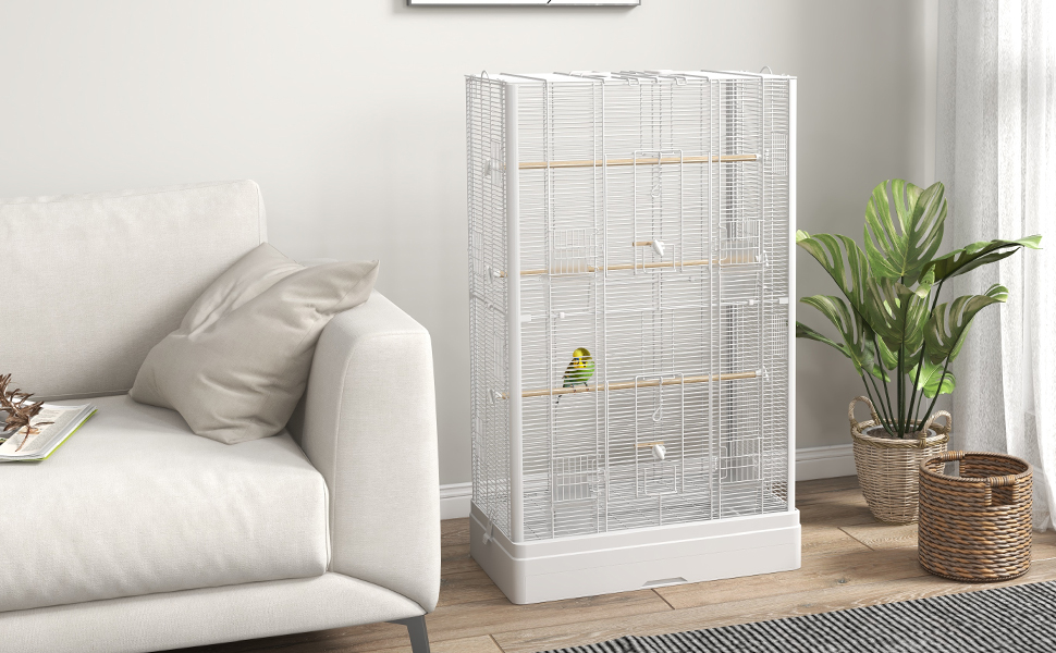 Großer, weißer Vogelkäfig in einem Wohnzimmer neben einem weißen Sofa. Kleiner grüner Vogel, der im Käfig sichtbar ist. Topfpflanze und geflochtener Korb in der Nähe