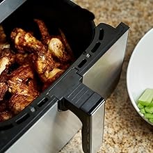 Close-up of seasoned chicken pieces cooking in a black air fryer basket with stainless steel housing visible.