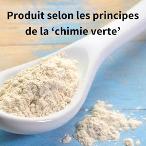 Cuillère en céramique blanche contenant un produit en poudre beige pâle, avec de la poudre supplémentaire dispersée sur une surface bleue, étiquetée comme produit principal de chimie verte.