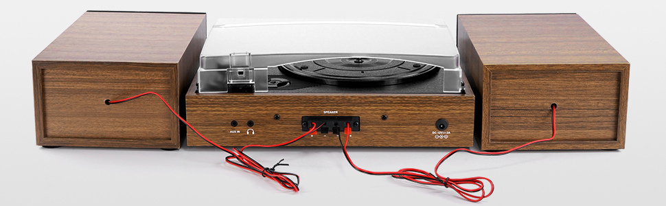 Vintage-style record player with wooden cabinet, turntable, and detached speakers. Red wires connect components. Control knobs and switches visible on front panel.