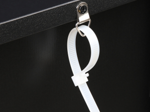 Nahaufnahme eines weißen Kabelclips oder Kabelorganisators aus Kunststoff, der an einer dunklen Oberfläche befestigt ist, wahrscheinlich zur Verwaltung von Kabeln oder Drähten