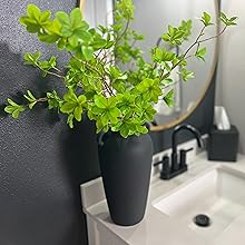 Artificial plants greenery in tall black ceramic vase being used as bathroom decor.