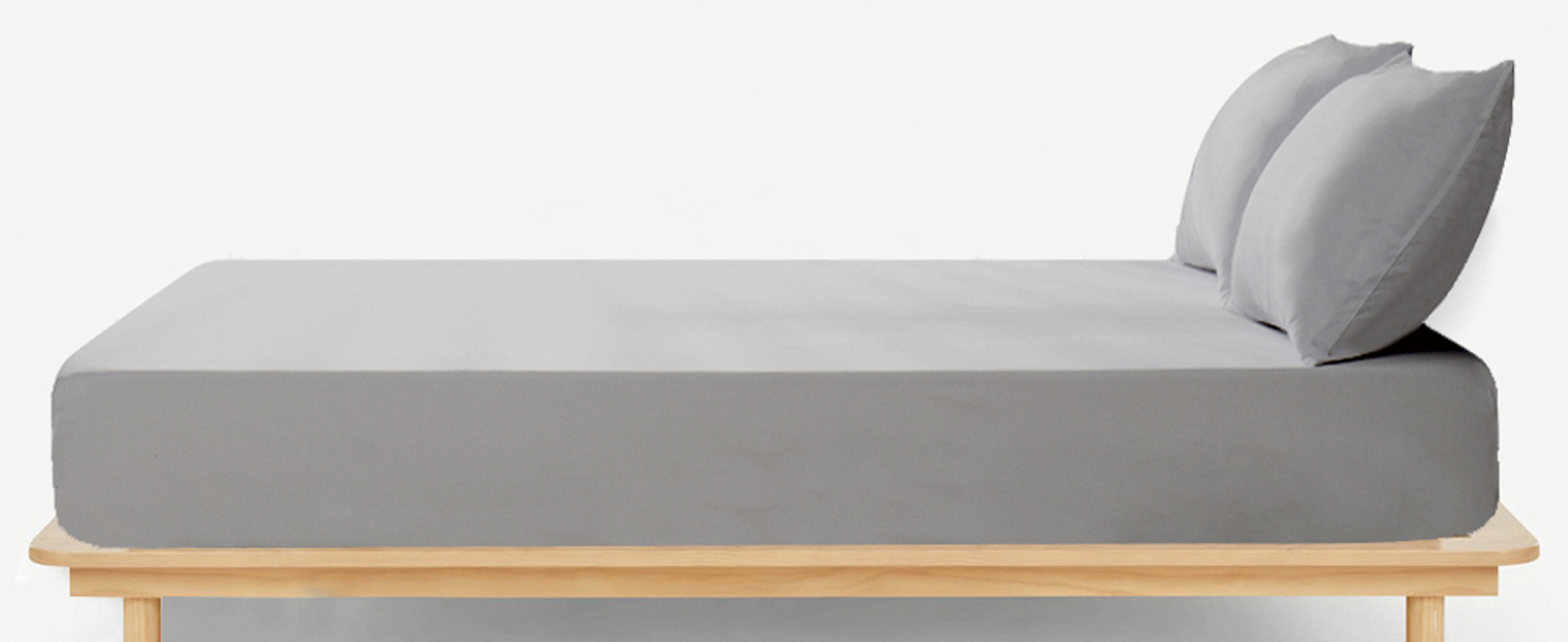 Modern gray daybed or chaise lounge with two large pillows on a light wooden platform base. Minimalist design with clean lines and neutral tones.