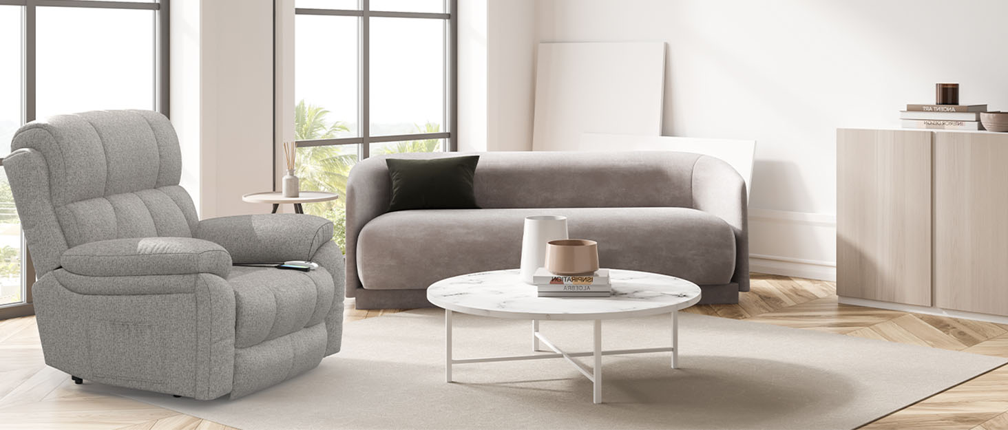 Modernes Wohnzimmer mit einem grauen Lehnsessel, einem geschwungenen Sofa, einem runden weißen Couchtisch und einem hellen Holzschrank vor weißen Wänden