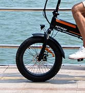 Primer plano de una rueda de bicicleta con neumáticos gruesos en una playa, con agua visible de fondo