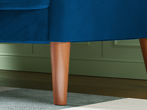 Brown finished wooden furniture leg attached to blue upholstered furniture against olive green wall trim