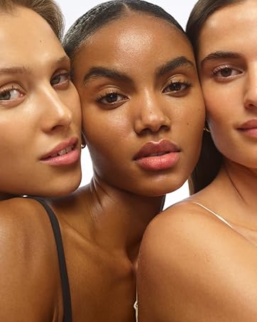 Close-up beauty portrait showcasing three models with natural, glowing makeup looks wearing neutral-toned tops.